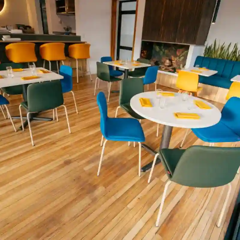 Mesas para restaurante en Quintana Roo — modelos redondos y cuadrados con cubierta blanca en restaurante moderno de Cancún, combinados con sillas tapizadas en azul y verde para espacios gastronómicos de alta rotación